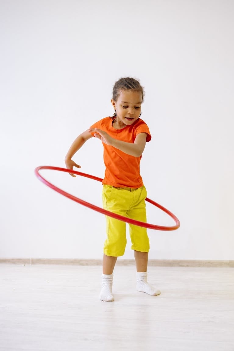 Energetic young girl hula hooping indoors in bright attire, enjoying playtime.
