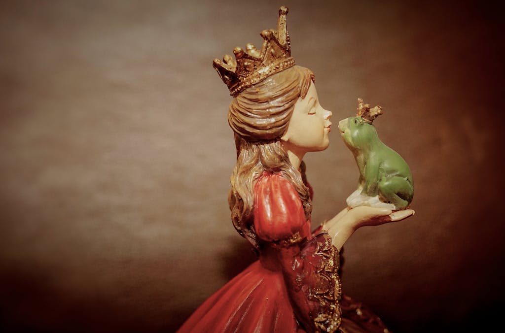 Side view of a ceramic princess figurine holding and kissing a crowned frog, evoking fairy tale magic.