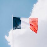 The French flag waving in the wind, set against a vibrant blue sky with clouds.